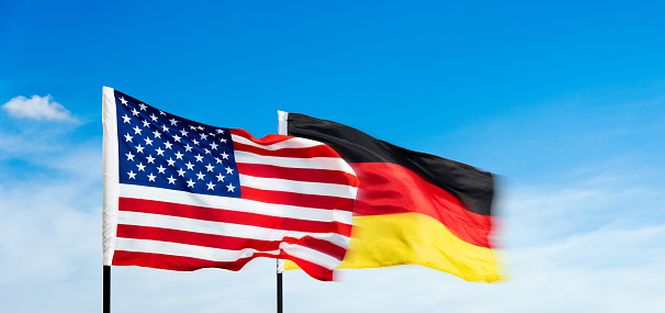 USA and German flags against blue sky background