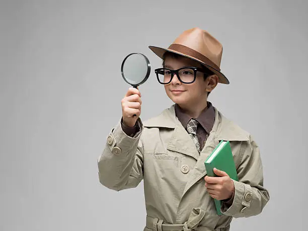 Little detective looking through magnifying glass on gray background