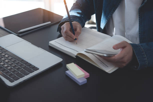 istock Event planner timetable agenda plan on year 2024 schedule event. Business woman checking planner on mobile phone, scheduling on calendar planner, laptop computer on office table 1764331866