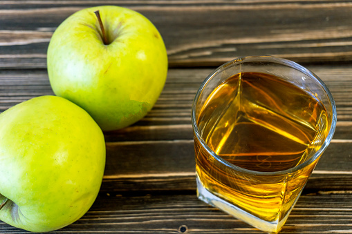 Green apples and glass with apple juice on wooden background