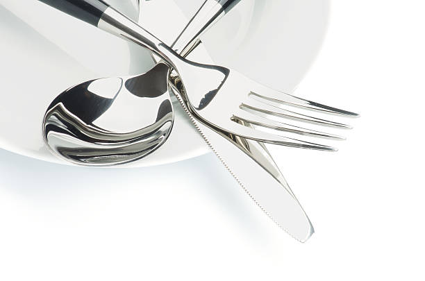 Silverware stacked in a pile on a white plate stock photo