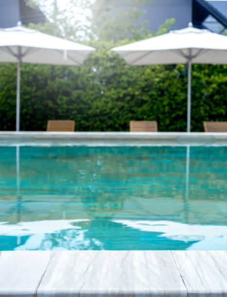 istock Summer pool background. Empty space on the pool edge, marble stone tiles and blurred swimming pool with beach umbrellas in tropical resort, summer background, vertical style. 1764380887
