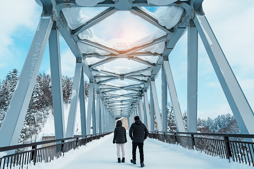 couple tourist Visiting in Biei, Traveler in Sweater sightseeing Shirahige Waterfall bridge with Snow in winter. landmark and popular for attractions in Hokkaido, Japan. Travel and Vacation concept
