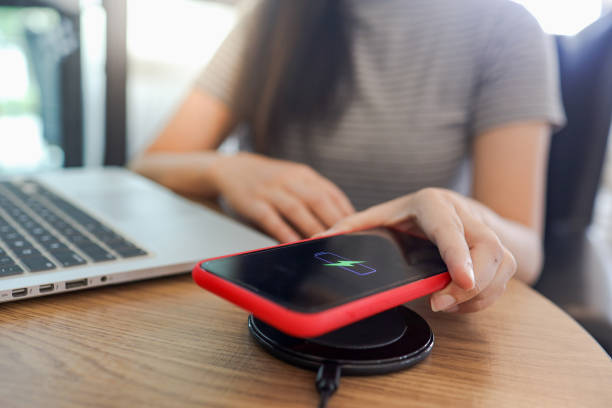 istock Charging mobile phone battery with wireless device in the table. Smartphone charging on a charging pad. Mobile phone near wireless charger. 1764429012