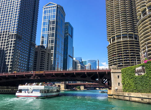 Tour boat on Chicago River passing under the State Street Bridge as tourist look up at surrounding skyscrapers. Chicago, Illinois, USA.