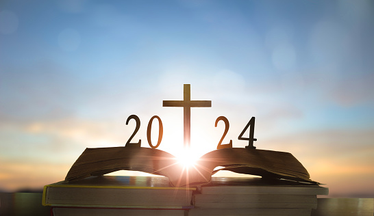 Año Nuevo 2024 y Cruz de Jesucristo en la Santa Biblia abierta con fondo de salida del sol photo