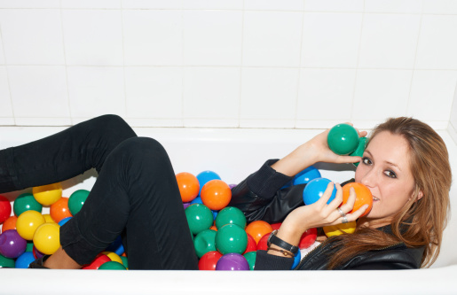 Attractive young hipster girl lying in a bath tub of colorful plastic balls
