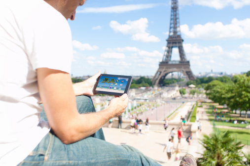 A male guy, having a look at his tablet PC in front of the fantastic Eiffel-Tower in Paris, France. Maybe he is checking weather information.