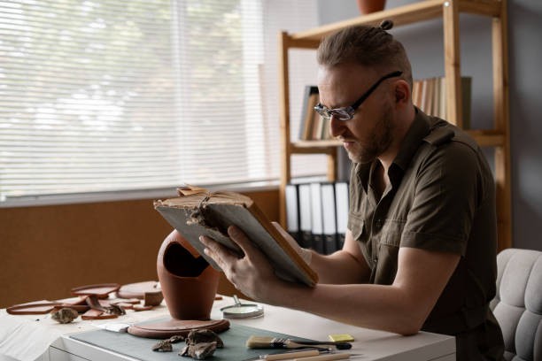 istock Archeologist works in office, reading old professional book, researching discovered ancient civilization cultural artifact. 1764500386