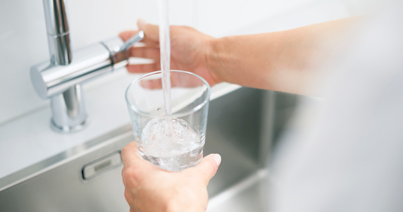 Woman filling glass of water in kitchen sink.