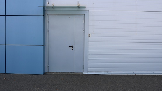 wall of a building made of gray and blue panels with a closed door as an urban abstract texture background with copy space, a side exit from a store or supermarket as an urban space without people