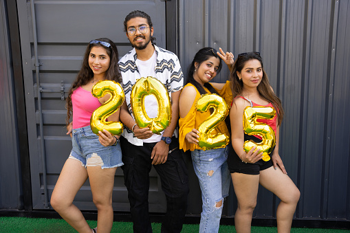 Happy group of indian friends with golden 2025 balloons outdoor. New Year celebration.