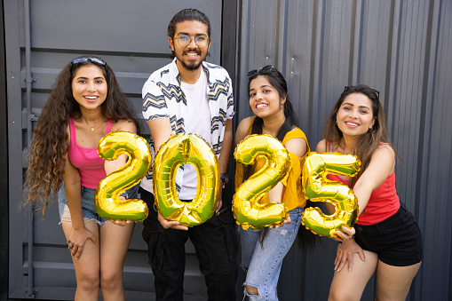 Happy group of indian friends with golden 2025 balloons outdoor. New Year celebration.