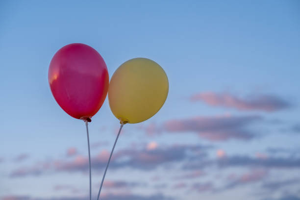 Two balloons, red and yellow against a blue sky with clouds illuminated by the setting sun.