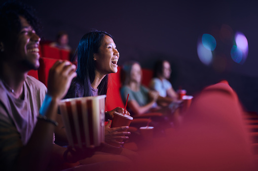 Cheerful Asian woman having fun while watching a movie in theatre.