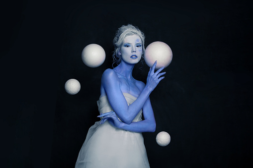 Stylish woman actress with stage makeup and hairstyle standing with white spheres on black banner background