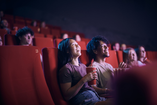 Happy Asian woman enjoying while watching a movie with other people in theatre.