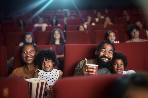 Happy African American family enjoying while watching a movie in cinema. Father is aiming at something.
