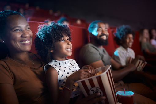 Happy African American girl and her mother watching a movie projection with their family in theatre.