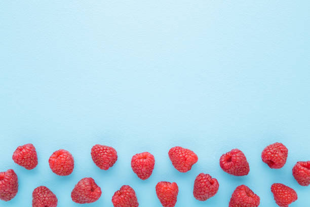 istock Fresh red raspberries on light blue table background. Pastel color. Closeup. Top down view. Empty place for text. 1764550056