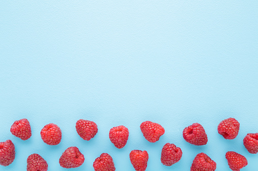 Fresh red raspberries on light blue table background. Pastel color. Closeup. Top down view. Empty place for text.