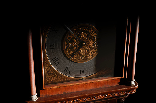 Close-up of the dial of an antique grandfather clock in a dark room, illuminated by light from the window.