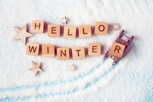 Wooden blocks with Hello Winter lettering on a snowy background. The concept of upcoming winter holiday season