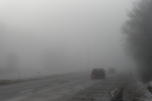 Cars on the road in the fog. Autumn and winter concept of dangerous traffic in bad weather. Car lights in bad visibility.