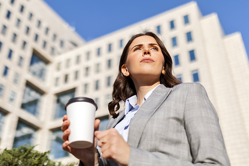 Businesswoman drinking coffee and using mobile phone in front of the office building