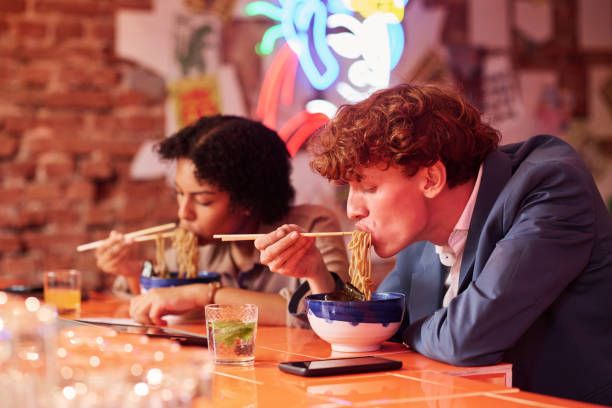 istock Young man with curly hair bending over table with bowl while eating ramen 1764639001