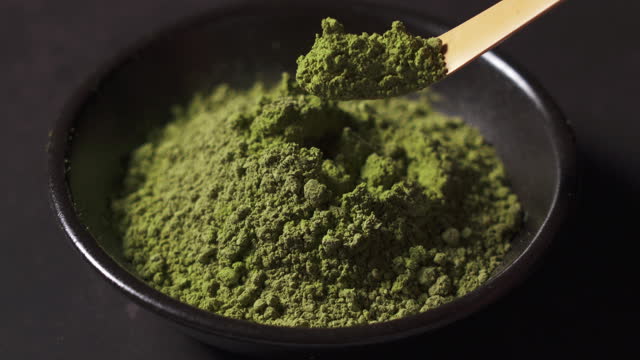 Scoop the matcha powder with a bamboo spoon placed against a dark background.