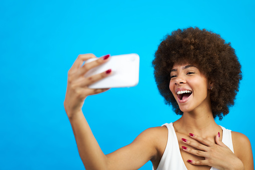 young latina woman with afro hair taking a picture with the mobile phone blue background