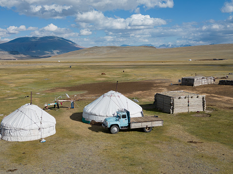 Elevated aerial view of a nomadic herder summer camp in the Altai Mountain Bayan-Olgii province of Western Mongolia. A parked truck is beside the family gers and wooden cabins where extended family live during the summer months. The nomadic herders migrate each season to different grazing areas with their livestock in the mountain region.