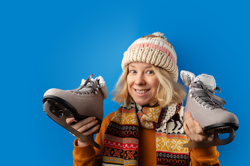 Woman preparing for ice skating, holding skates on a blue background, figure skating equipment