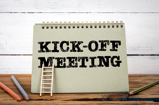 Kick off meeting. Green notepad on wooden texture table and white background.