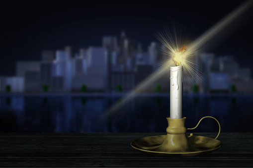 Lit candle with spark. In the background the city at night.