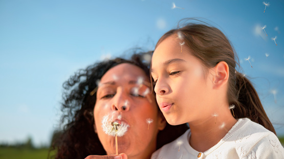 Close-up of mother and daughter blowing dandelion seeds.