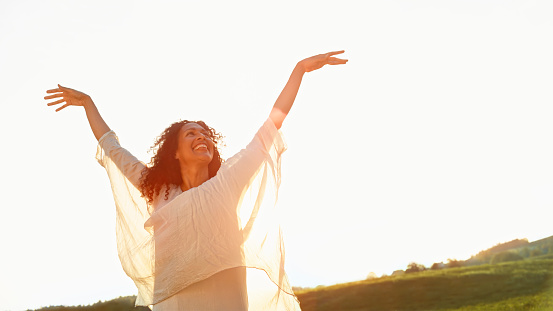 Smiling mature woman standing with arms raised in meadow.