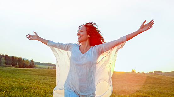 Smiling mature woman standing with arms outstretched in meadow.