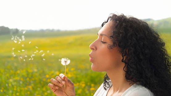 Side view of mature woman blowing dandelion seeds in meadow.