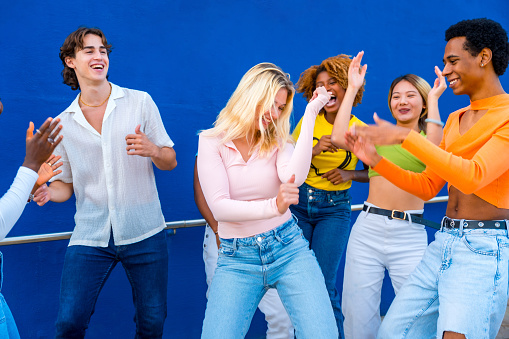 Blonde young woman dancing in a dance battle with friends with a blue wall as background