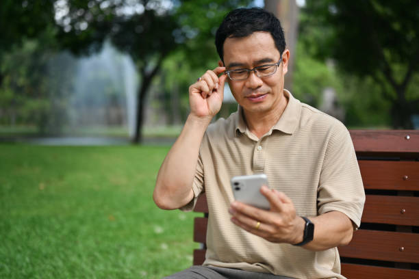 istock Smiling middle age man wearing glasses using mobile phone in the public park. 1764668100