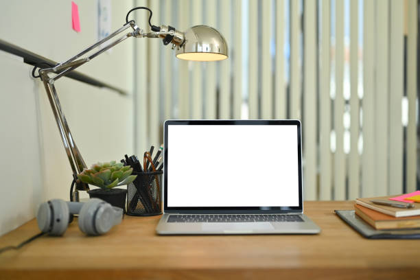 istock Front view of laptop computer with white screen, headphone, book and lamp on wooden table 1764668681