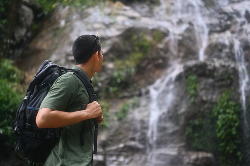 Image of male hiker with backpack enjoying the view of beautiful tropical waterfall.