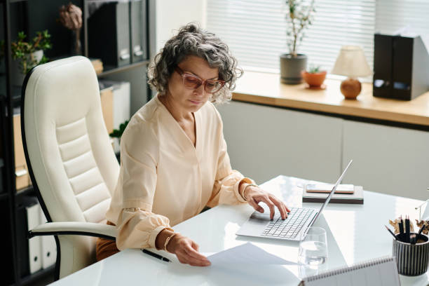 istock Mature female employer looking through paper document and typing 1764679752