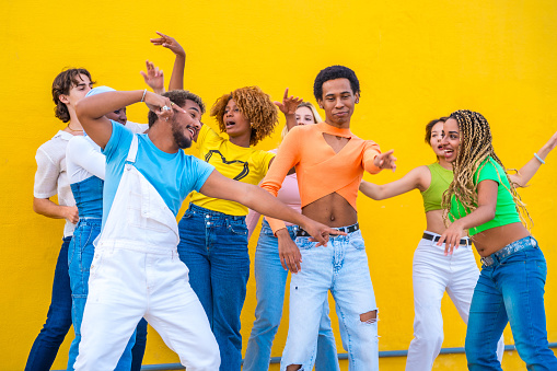 Multicultural group of happy young people dancing together in a yellow urban space