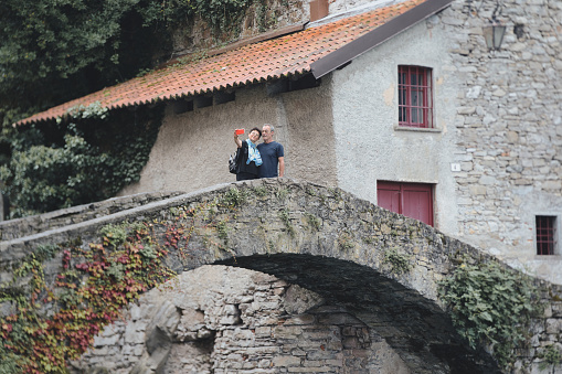 Retired couple taking a vacation selfie on the Roman stone bridge in Nesso, Como province, Lombardy, Italy.
