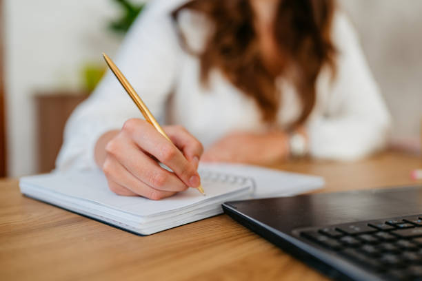 istock Young Woman Writing In A Notebook While Working On A Laptop At The Kitchen Table 1764695765