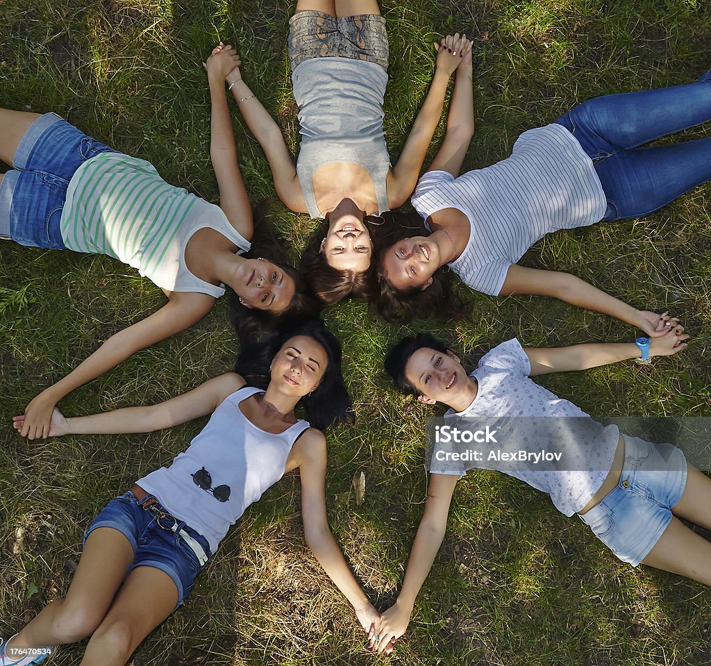 Natural friendship Five female teenagers are lying on the grass forming the star-shape by their bodies and hands. They keep hands of each other, smiling and enjoying the nature, friendship and relax. Summer Camp Stock Photo