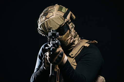Photo of a confident and courageous military man on a dark isolated background in a camouflage uniform and with a weapon. The concept of a strong and invincible army.